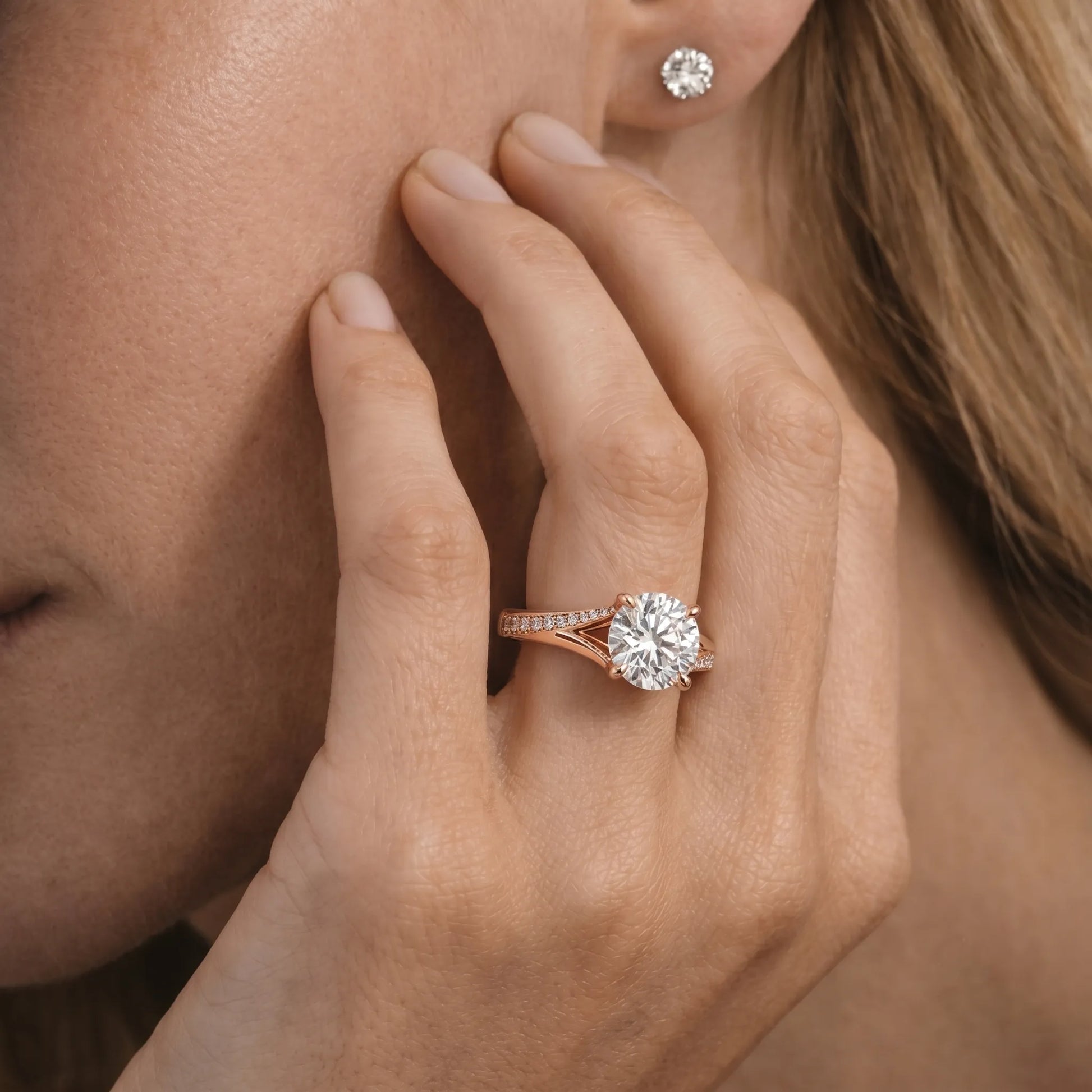 Close-up of a hand wearing a rose gold ring with a diamond, touching the cheek.