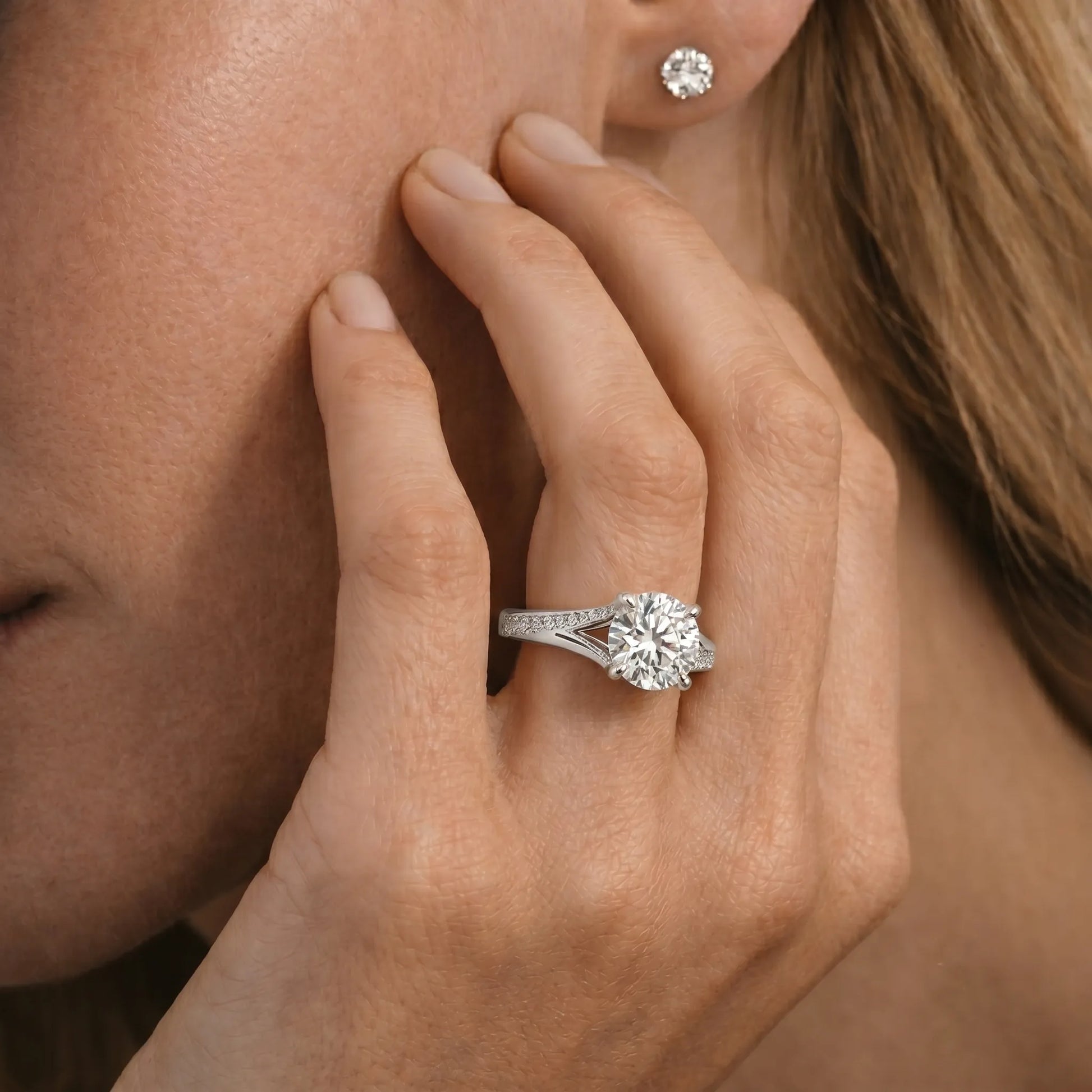 Close-up of a hand wearing a white gold  ring and diamond earring, touching the cheek.