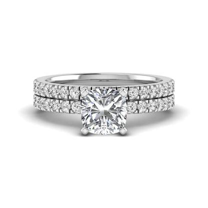 Cushion cut lab grown diamond bridal ring set featuring a four-prong solitaire engagement ring with a matching pavé diamond wedding band in a white gold tone design.