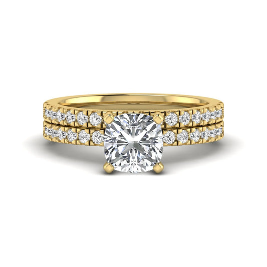 Cushion cut lab grown diamond bridal ring set featuring a four-prong solitaire engagement ring with a matching pavé diamond wedding band in a yellow gold tone design.
