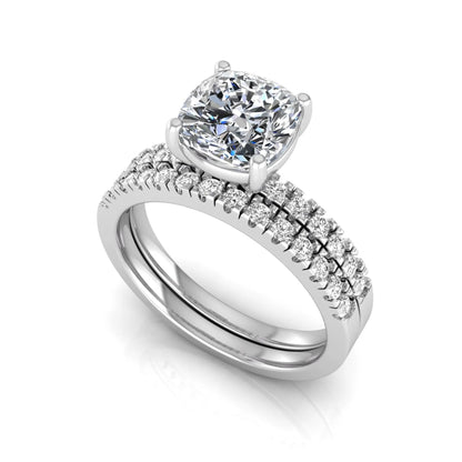Cushion cut lab grown diamond bridal ring set featuring a four-prong solitaire engagement ring with pavé round diamond accents and matching wedding band in white gold finish.