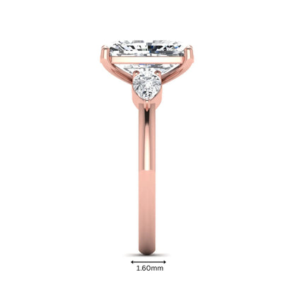 Elongated cushion cut lab grown diamond three stone engagement ring featuring pear cut side diamonds in a four-prong setting with a polished rose gold tone band.