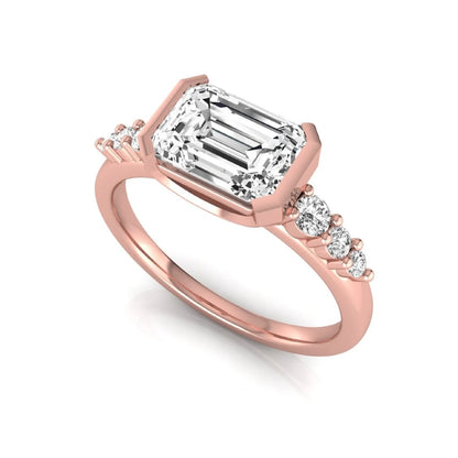 Emerald cut lab grown diamond engagement ring featuring a horizontal east-west bezel-set center diamond with graduated round side diamonds in a rose gold tone.