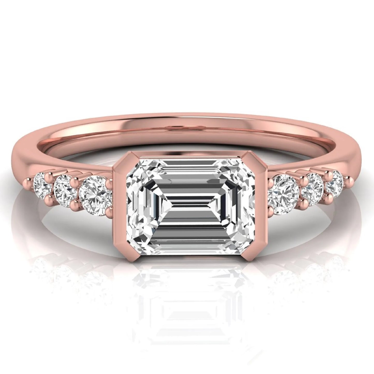 Emerald cut lab grown diamond engagement ring featuring a horizontal east-west bezel-set center diamond with graduated round side diamonds in a rose gold tone.