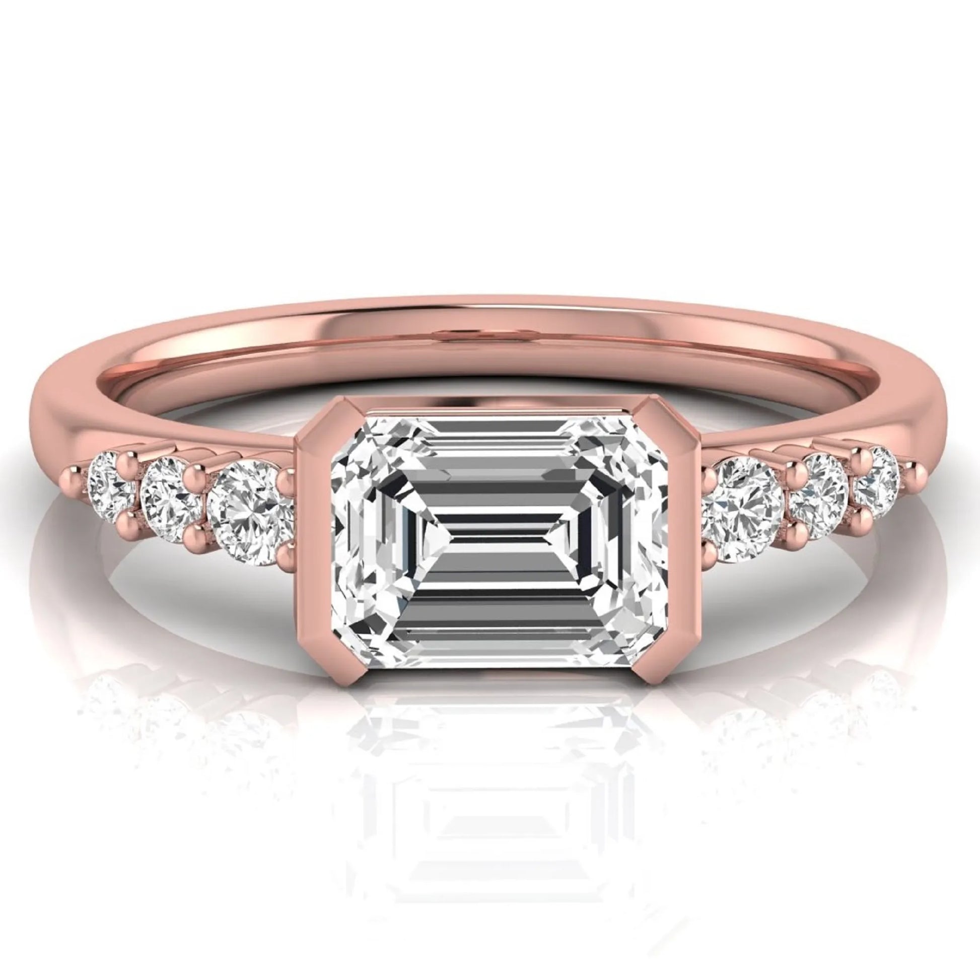 Emerald cut lab grown diamond engagement ring featuring a horizontal east-west bezel-set center diamond with graduated round side diamonds in a rose gold tone.
