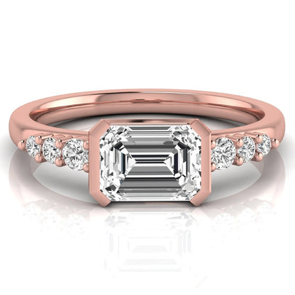 Emerald cut lab grown diamond engagement ring featuring a horizontal east-west bezel-set center diamond with graduated round side diamonds in a rose gold tone.