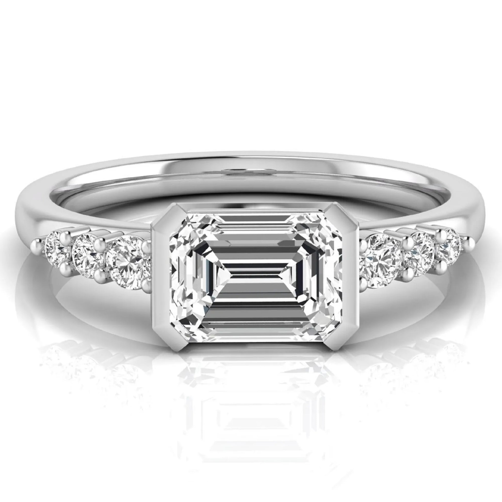 Emerald cut lab grown diamond engagement ring featuring a horizontal east-west bezel-set center diamond with graduated round side diamonds in a white gold tone.