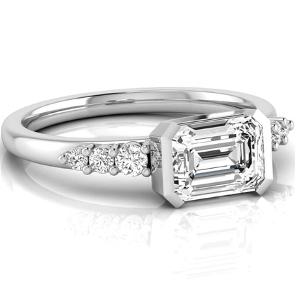 Emerald cut lab grown diamond engagement ring featuring a horizontal east-west bezel-set center diamond with graduated round side diamonds in a white gold tone.