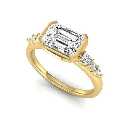 Emerald cut lab grown diamond engagement ring featuring a horizontal east-west bezel-set center diamond with graduated round side diamonds in a yellow gold tone.