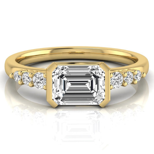 Emerald cut lab grown diamond engagement ring featuring a horizontal east-west bezel-set center diamond with graduated round side diamonds in a yellow gold tone.