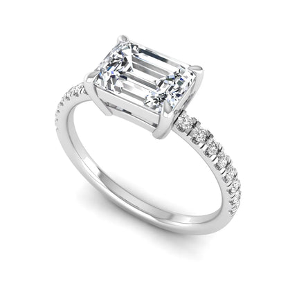 Emerald cut lab grown diamond solitaire pavé engagement ring with four-prong setting and white gold tone band.