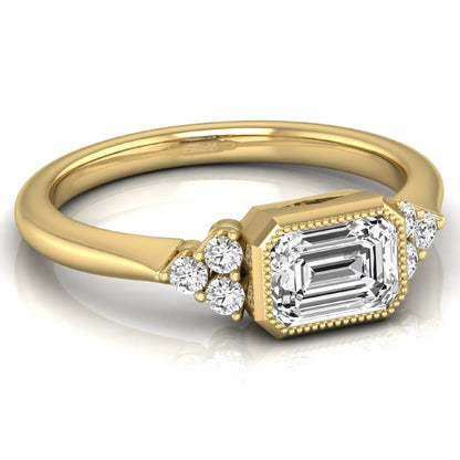 Emerald cut lab grown diamond engagement ring featuring a milgrain bezel setting with round side stone clusters in yellow gold.