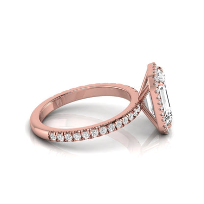 Emerald cut lab grown diamond engagement ring featuring a round diamond halo, pavé accent band, and four-prong setting with a polished rose gold tone band.