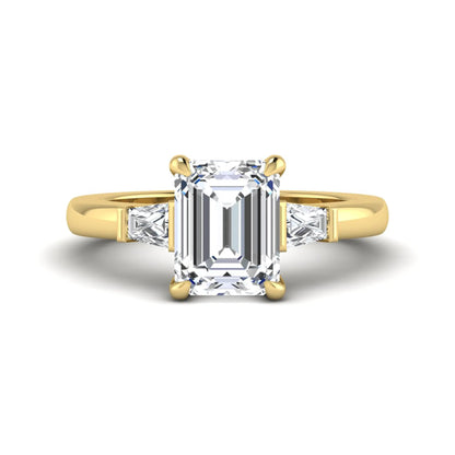 Emerald cut lab grown diamond three-stone engagement ring featuring tapered baguette side diamonds in a classic four-prong yellow gold style setting.