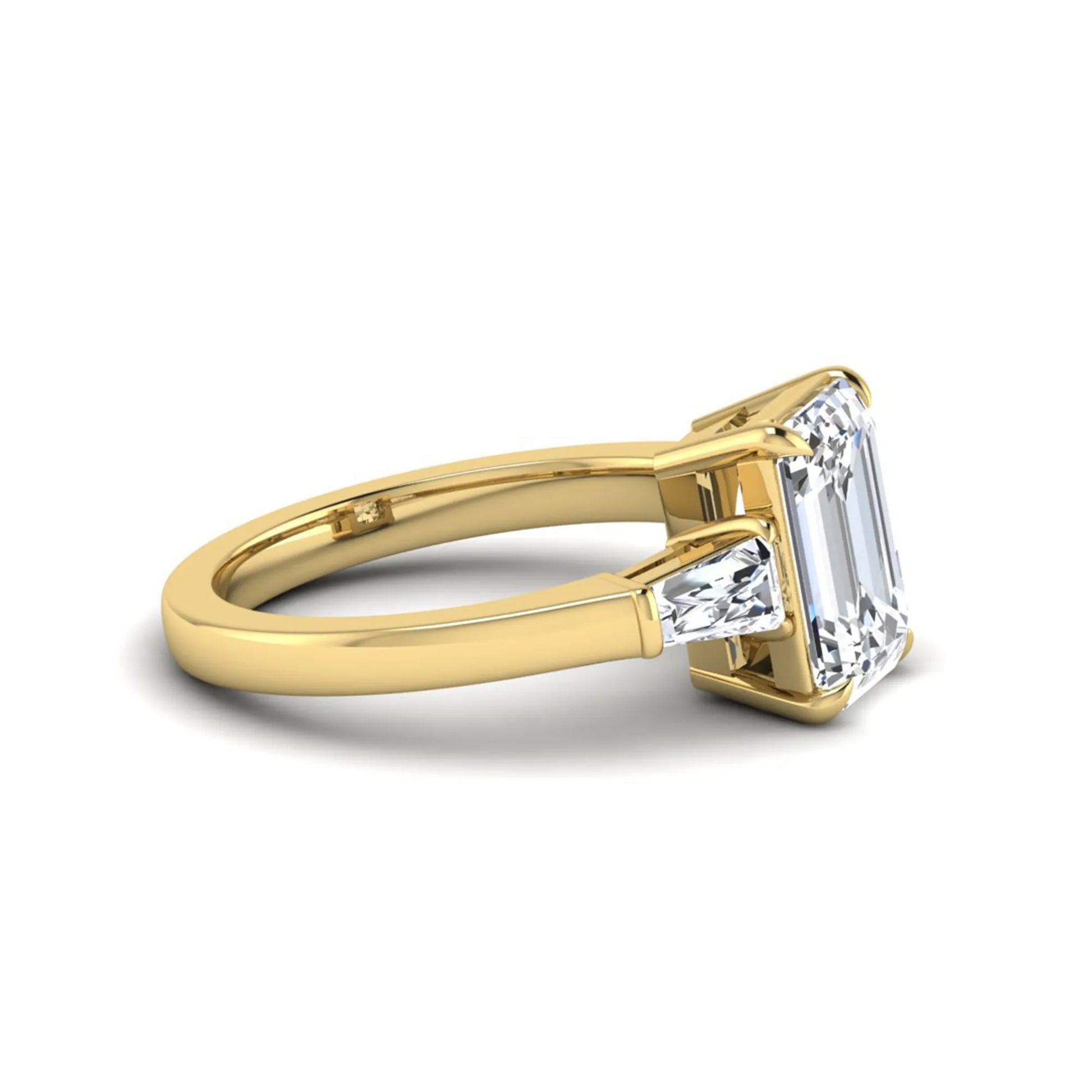 Emerald three stone prong set lab grown diamond engagement ring featuring a 3.00 carat emerald cut center diamond with tapered baguette side diamonds in yellow gold finish.
