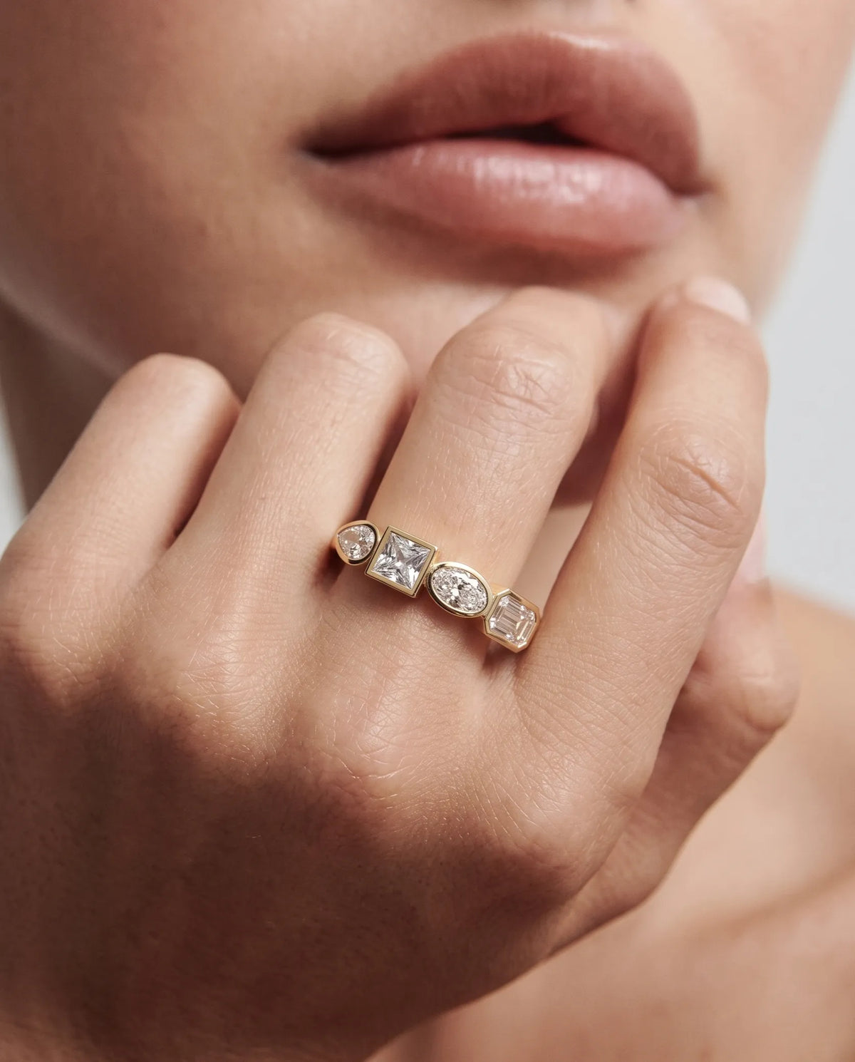 A close-up of a model's hand wearing a delicate yellow gold ring with a row of clear gemstones, including a marquise-cut center stone.