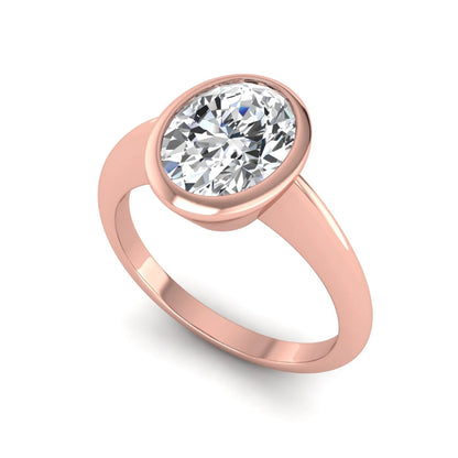 Oval cut lab grown diamond solitaire engagement ring in a bezel setting with a rose gold tone minimalist band.