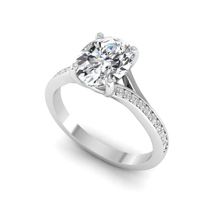 Oval cut lab grown diamond split shank pavé engagement ring with four-prong setting and white gold tone band.