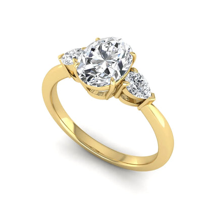 Oval cut lab grown diamond three stone engagement ring with pear cut side diamonds and prong setting in yellow gold tone.