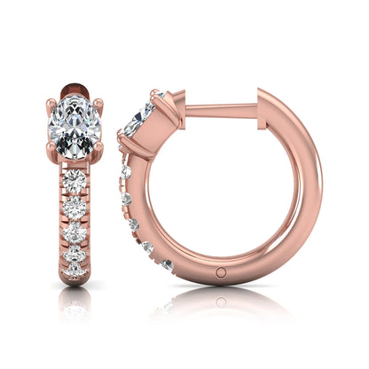 Oval cut lab grown diamond huggie hoop earrings featuring a four prong basket set center diamond with graduated round brilliant pavé diamonds on a rose gold hoop.