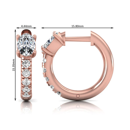 Oval cut lab grown diamond huggie hoop earrings featuring a four prong basket set center diamond with graduated round brilliant pavé diamonds on a rose gold hoop.