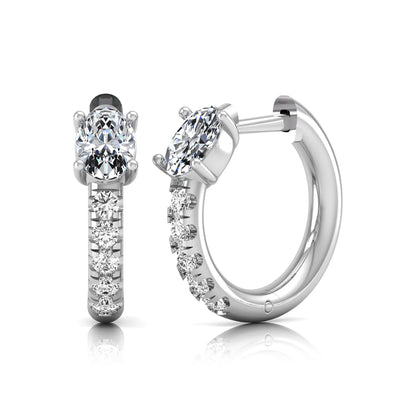 Oval cut lab grown diamond huggie hoop earrings featuring a four prong basket set center diamond with graduated round brilliant pavé diamonds on a white gold hoop.