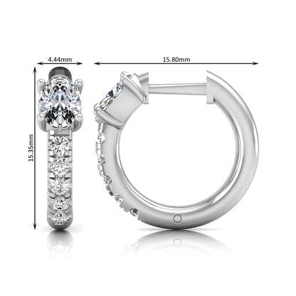 Oval cut lab grown diamond huggie hoop earrings featuring a four prong basket set center diamond with graduated round brilliant pavé diamonds on a white gold hoop.