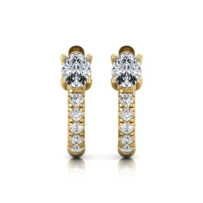 Oval cut lab grown diamond huggie hoop earrings featuring a four prong basket set center diamond with graduated round brilliant pavé diamonds on a yellow gold hoop.