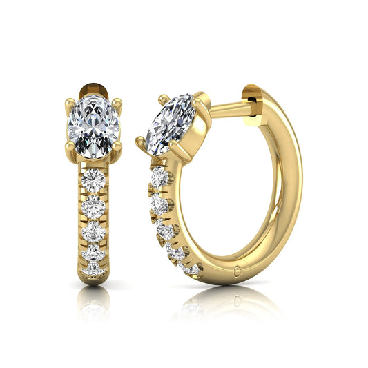 Oval cut lab grown diamond huggie hoop earrings featuring a four prong basket set center diamond with graduated round brilliant pavé diamonds on a yellow gold hoop.
