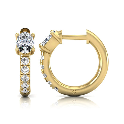 Oval cut lab grown diamond huggie hoop earrings featuring a four prong basket set center diamond with graduated round brilliant pavé diamonds on a yellow gold hoop.