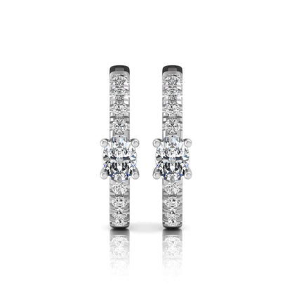 Oval and round lab grown diamond pavé huggie hoop earrings featuring a four prong oval center diamond with graduated shared prong round diamond accents in white gold.