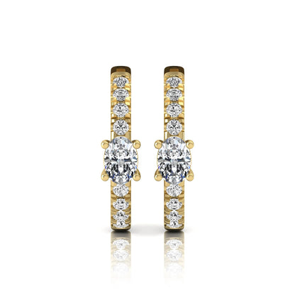 Oval and round lab grown diamond pavé huggie hoop earrings featuring a four prong oval center diamond with graduated shared prong round diamond accents in yellow gold.