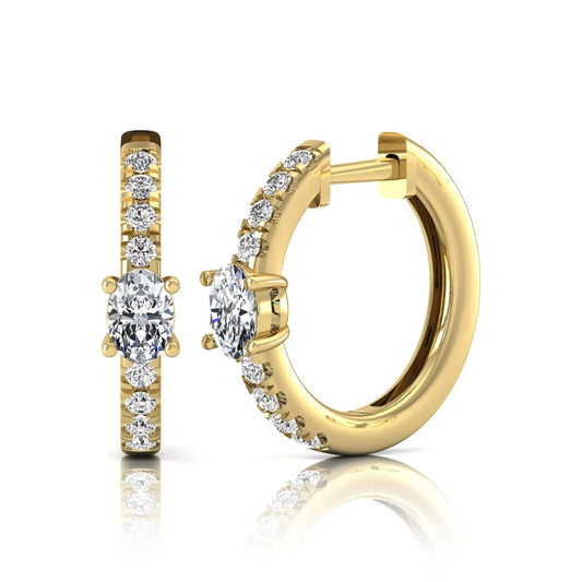 Oval and round lab grown diamond pavé huggie hoop earrings featuring a four prong oval center diamond with graduated shared prong round diamond accents in yellow gold.