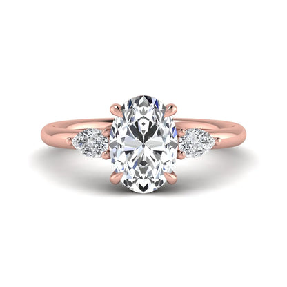 Oval cut lab grown diamond three stone engagement ring with pear cut side diamonds in a prong setting on a polished rose gold band.