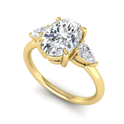 Oval cut lab grown diamond three stone engagement ring with pear cut side diamonds in a prong setting on a polished yellow gold band.