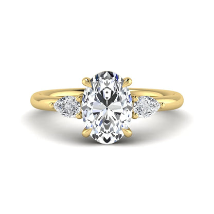 Oval cut lab grown diamond three stone engagement ring with pear cut side diamonds in a prong setting on a polished yellow gold band.