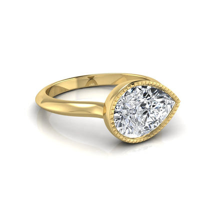Pear cut lab grown diamond solitaire engagement ring featuring a milgrain bezel setting with a yellow gold tone band.