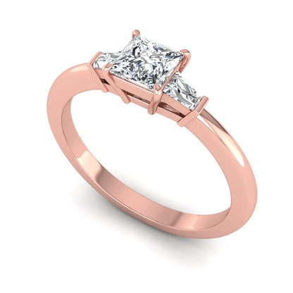 Princess cut lab grown diamond three stone engagement ring with tapered baguette side diamonds in a four-prong setting and rose gold tone band.