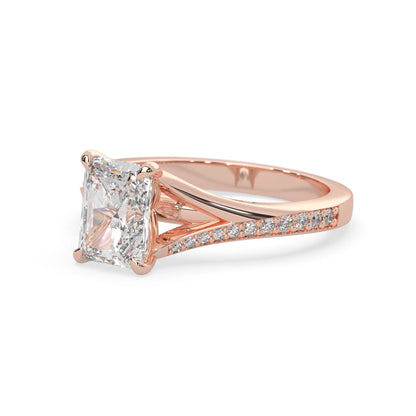 Rose gold ring with an emerald cut lab grown diamond and smaller diamonds on the band against a white background