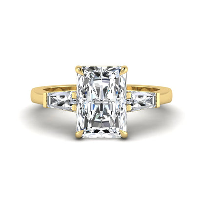 Radiant cut lab grown diamond three stone engagement ring with tapered baguette side diamonds and four prong setting in yellow gold tone.