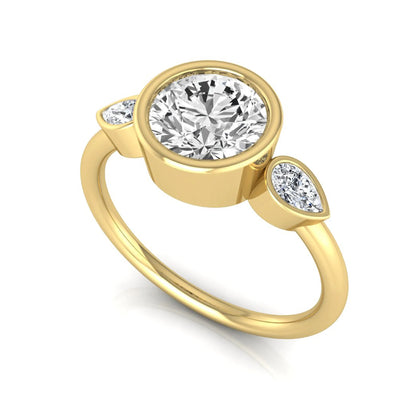 Round cut lab grown diamond bezel three stone engagement ring featuring a 1.28 carat IGI certified center diamond with pear cut side diamonds in yellow gold.