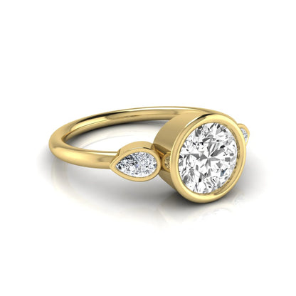 Round cut lab grown diamond bezel three stone engagement ring featuring a 1.28 carat IGI certified center diamond with pear cut side diamonds in yellow gold.