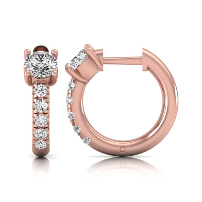 Round brilliant lab grown diamond huggie hoop earrings featuring an elevated four prong center diamond with graduated shared prong pavé round diamond accents in rose gold.