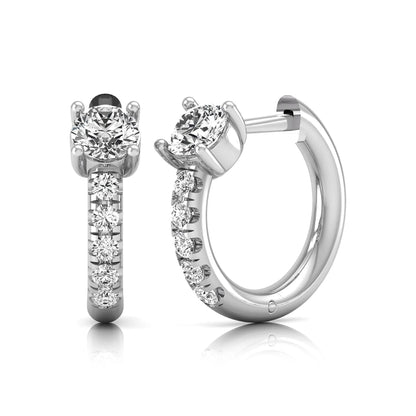 Round brilliant lab grown diamond huggie hoop earrings featuring an elevated four prong center diamond with graduated shared prong pavé round diamond accents in white gold.