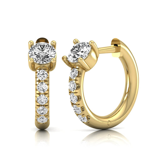 Round brilliant lab grown diamond huggie hoop earrings featuring an elevated four prong center diamond with graduated shared prong pavé round diamond accents in yellow gold.