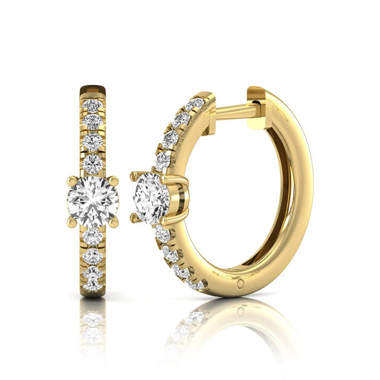 Round brilliant lab grown diamond pavé huggie hoop earrings featuring a four prong center diamond with graduated shared prong pavé round diamonds in yellow gold.