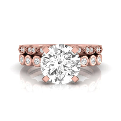 Round cut lab grown diamond bridal ring set featuring a four-prong solitaire engagement ring with a matching side stone wedding band accented by round bezel-set diamonds and vintage milgrain detailing in rose gold