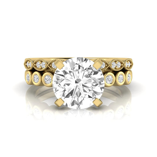 Round cut lab grown diamond bridal ring set featuring a four-prong solitaire engagement ring with a matching side stone wedding band accented by round bezel-set diamonds and vintage milgrain detailing in yellow gold