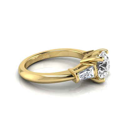 Round cut lab grown diamond three-stone engagement ring featuring tapered baguette side diamonds in a classic four-prong yellow gold setting.
